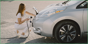 Coface Focus: Will the electric vehicle metals boom last? The photo shows a woman connecting an electric car to an energy source.